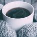 A mug being held by someone wearing mittens, representing some of the pros and cons of the winter lifestyle. By Alex Padurariu.